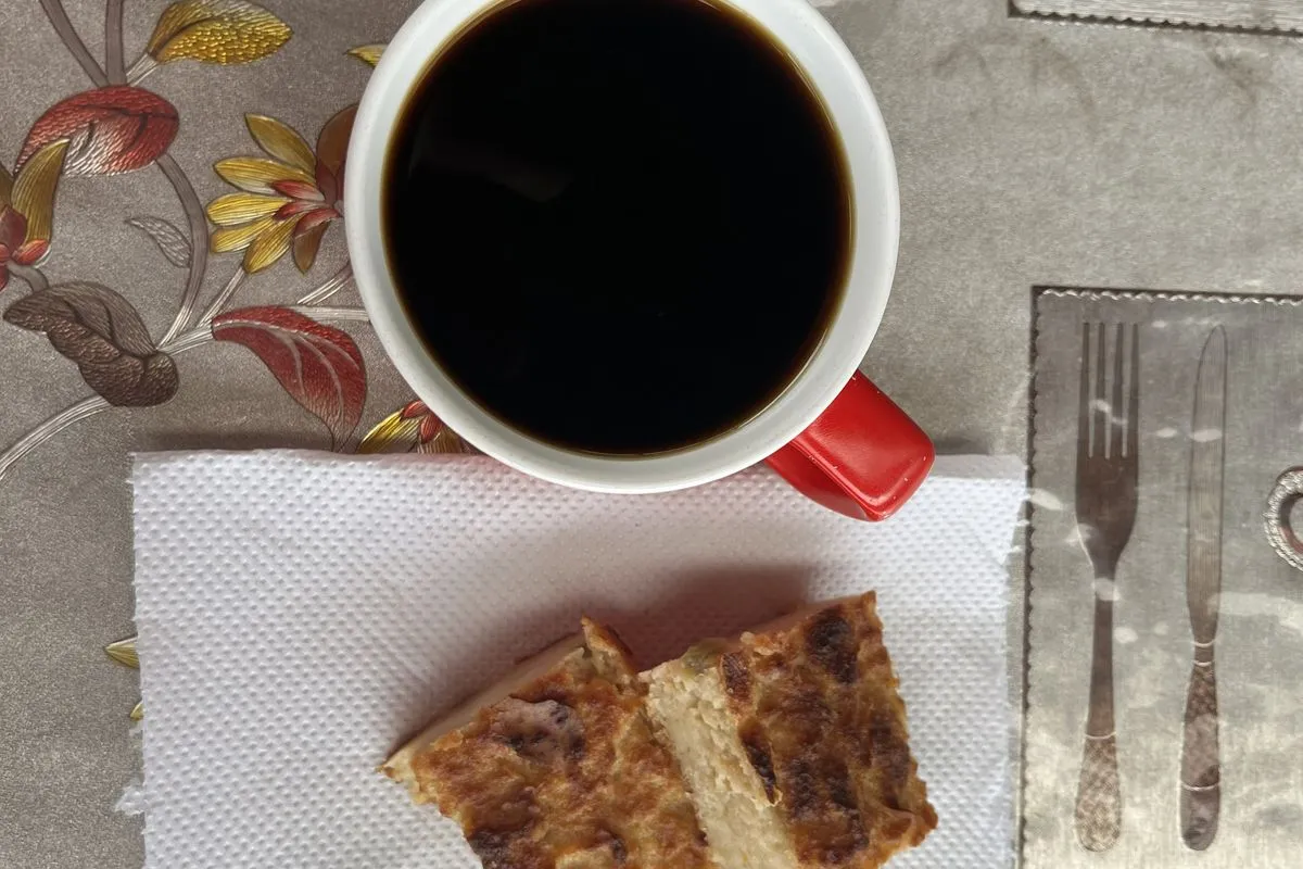Overhead view of a red-handled mug of black coffee and two slices of toasted bread on a napkin, on a floral tablecloth.