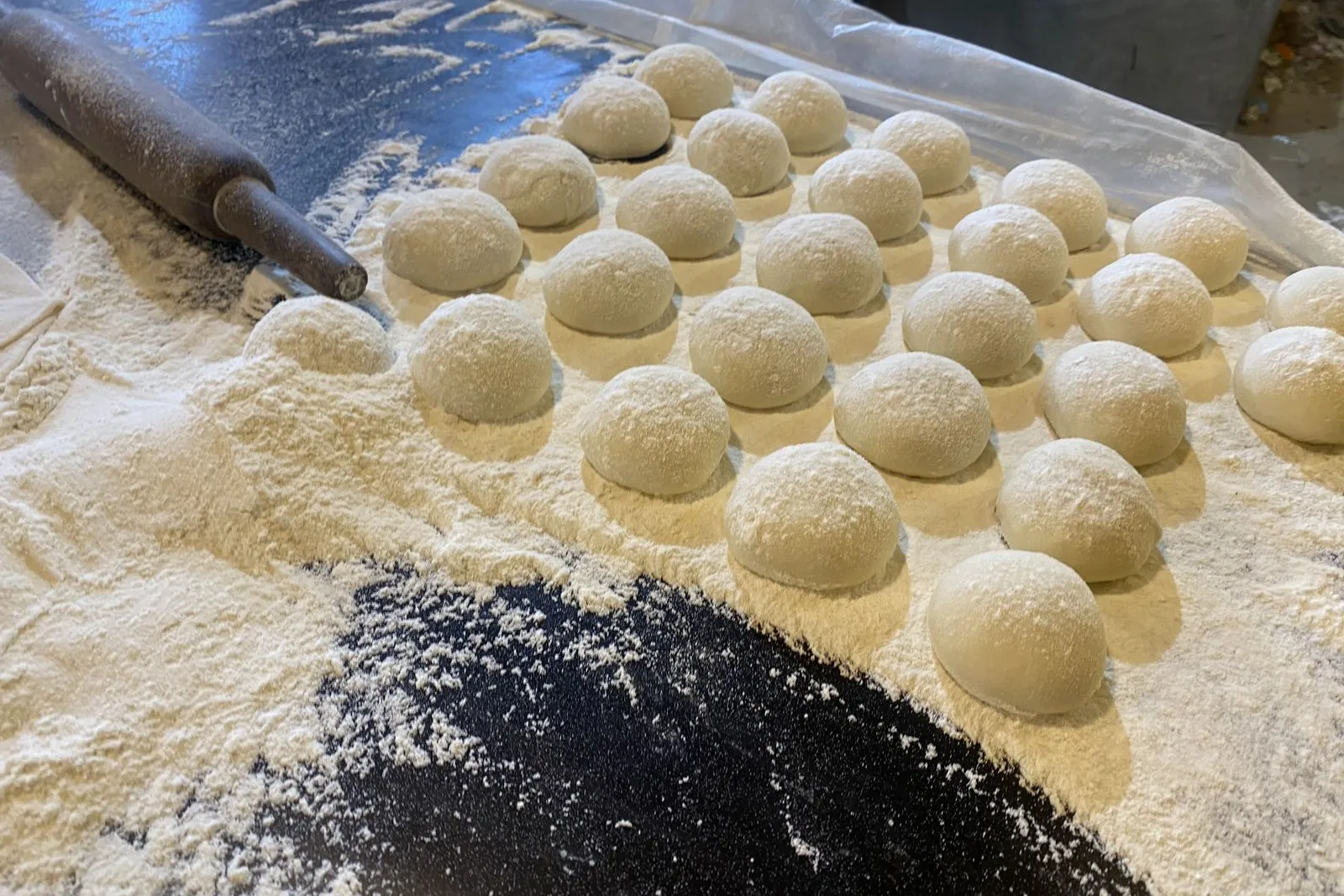 Rows of floured dough rounds resting on a floured worktop beside a wooden rolling pin.